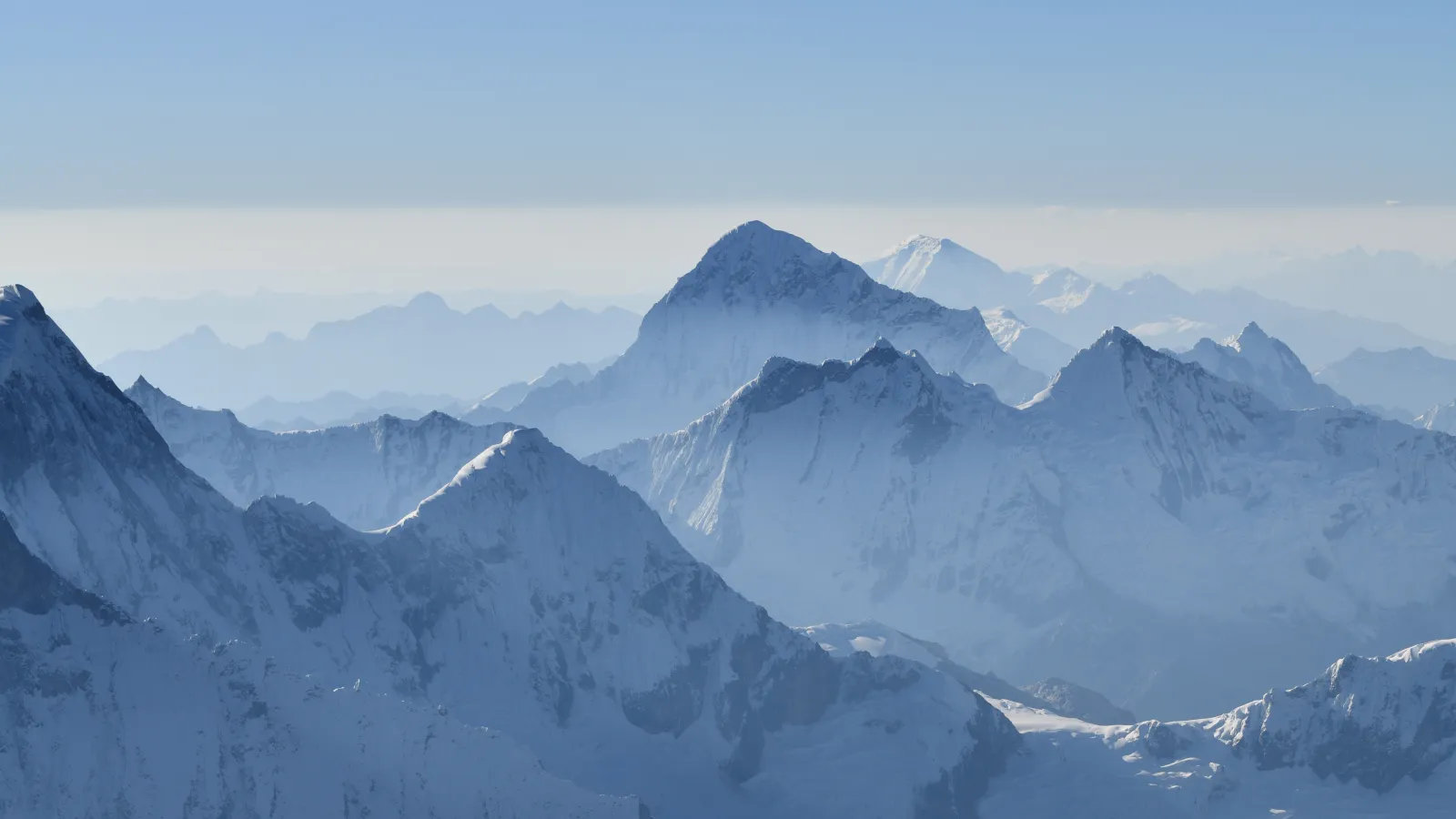 snow covered jagged mountain peaks under clear blue skies above but some haze below