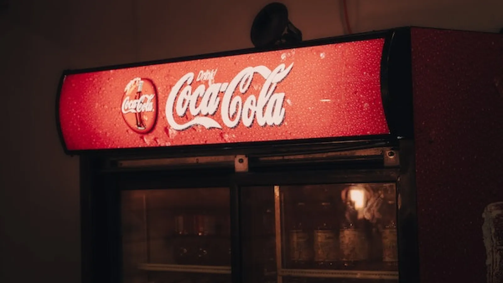 Coca-Cola Vending Machine with red sign back-lit in a dark room.