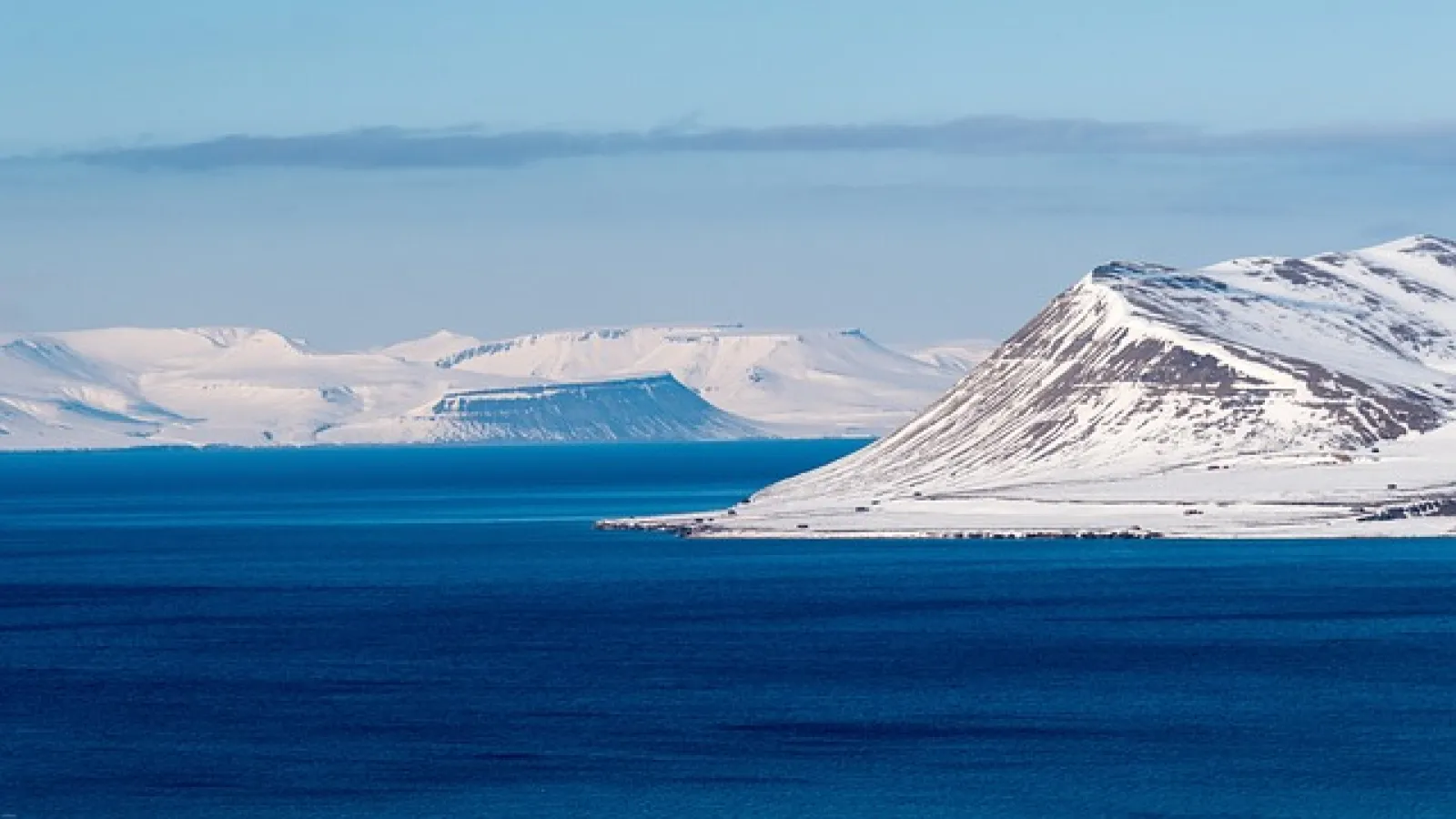 Scenic view of a body of water and snow-covered mountain and ice in blue waters under blue skies with clouds.