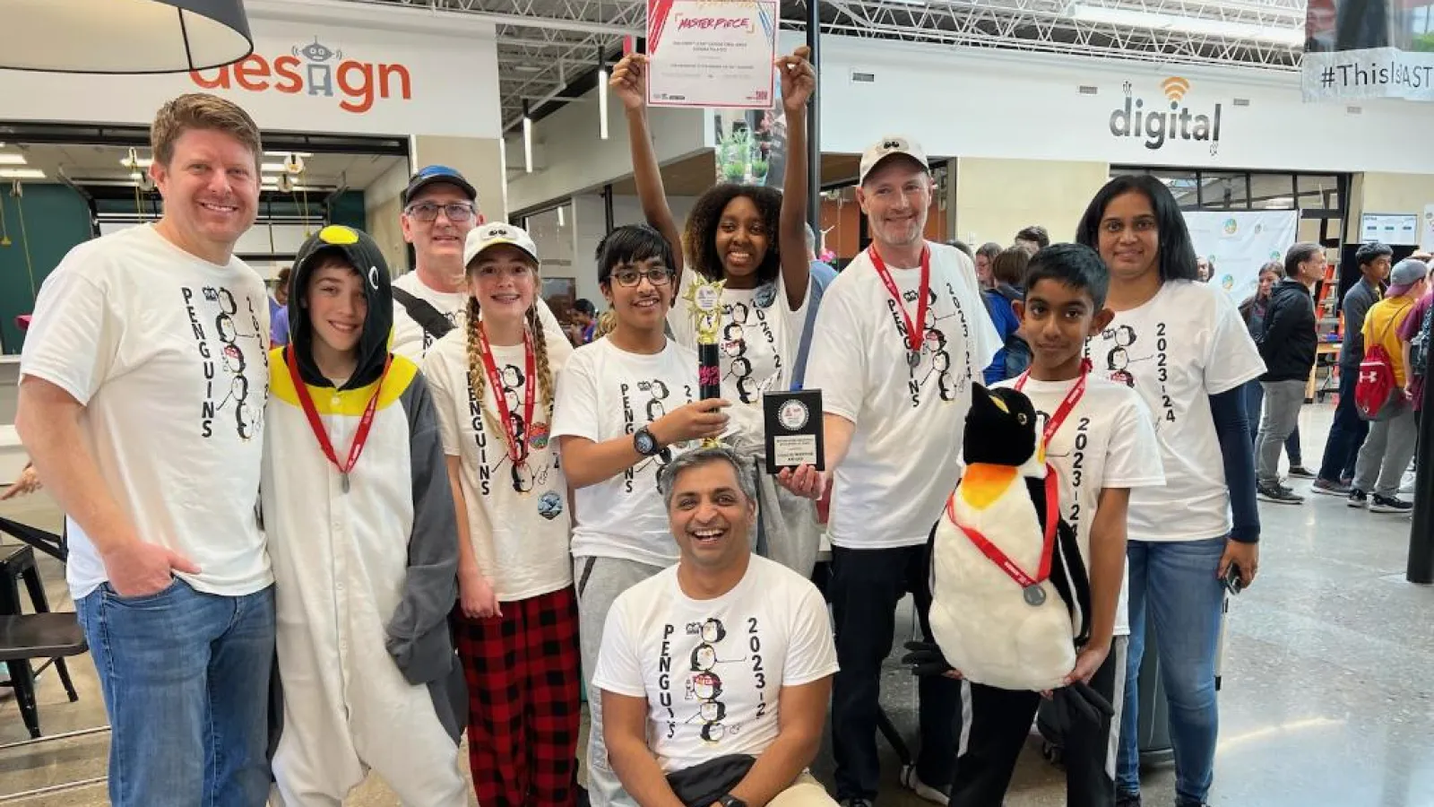 A group of youth with medals and adults posing indoor with one youth holding a trophy and one a paper and an adult holding a plaque,