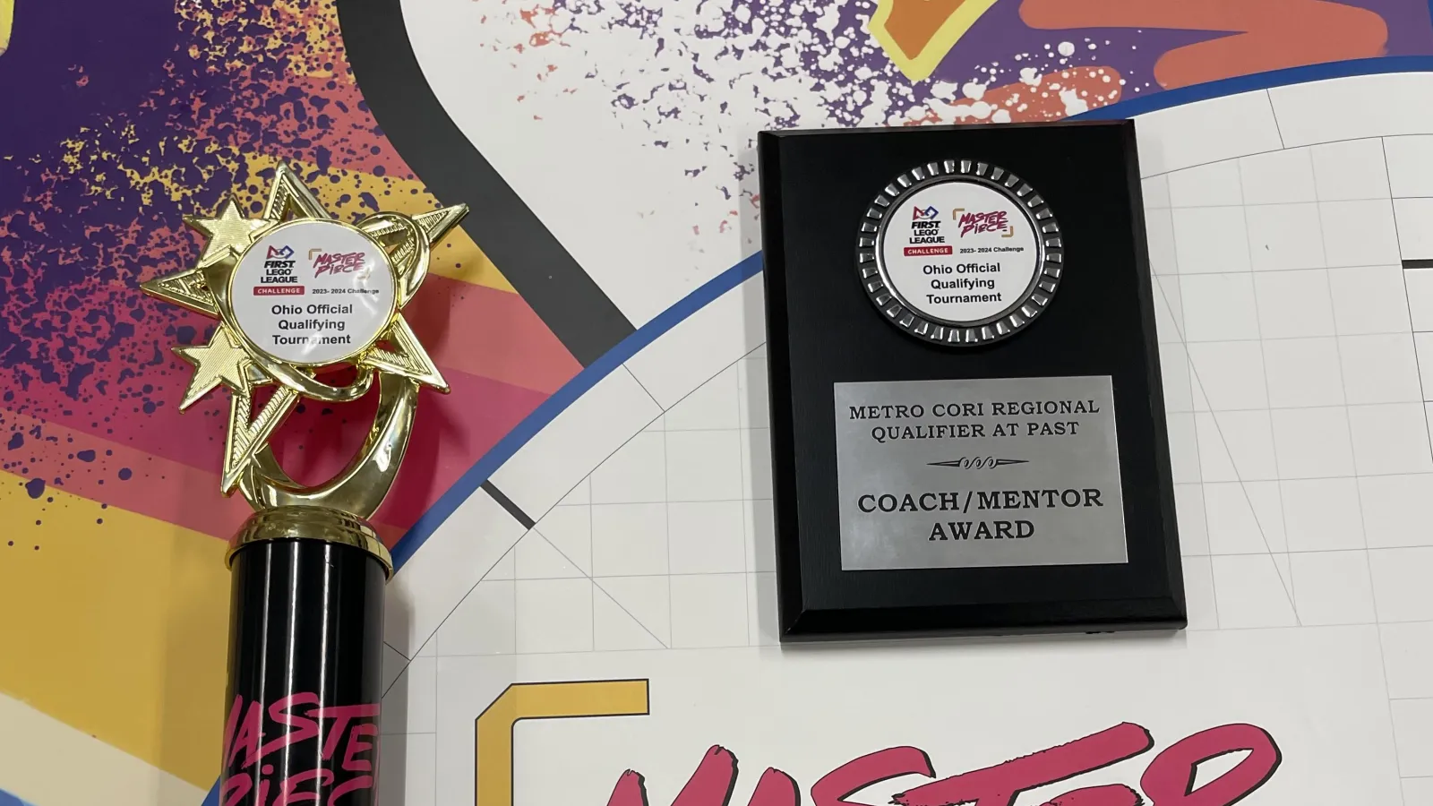 A trophy and a plaque on a table with colorful images and text saying Master Piece.