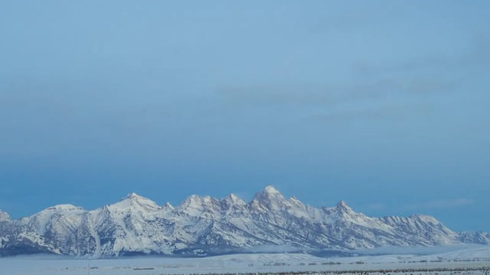 Snow covered ground and mountains in a distance under blue skies.