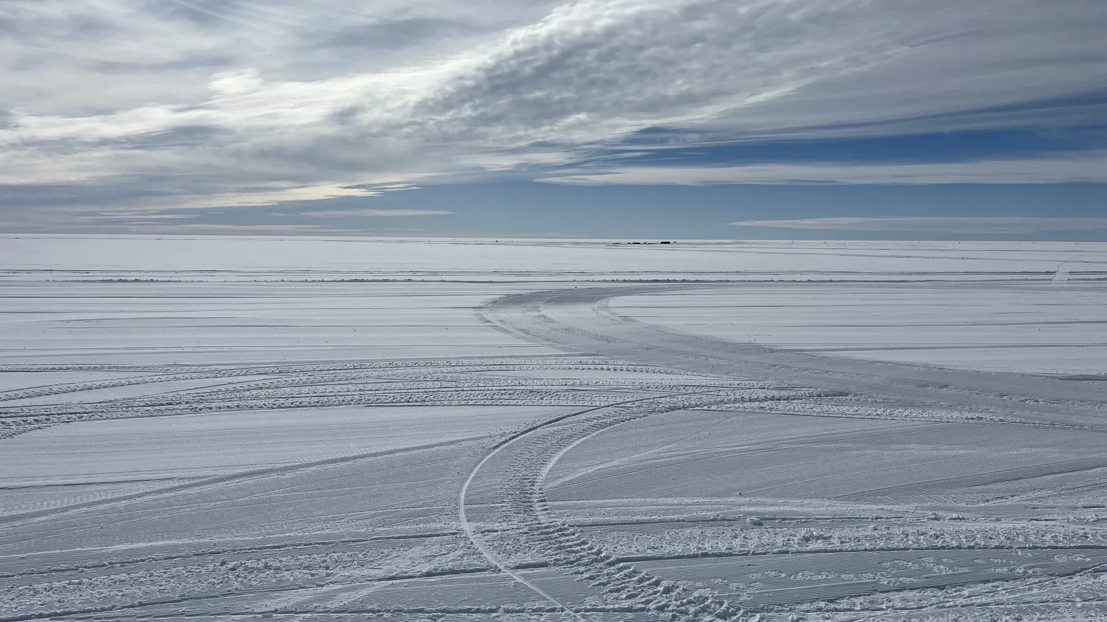 Vast field of snow under blue skies with white clouds.