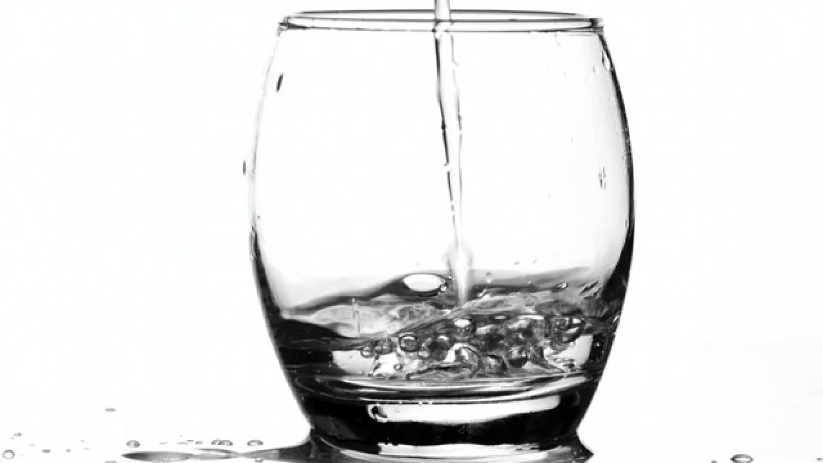 Clear liquid pouring into a clear glass cup on a white background. 