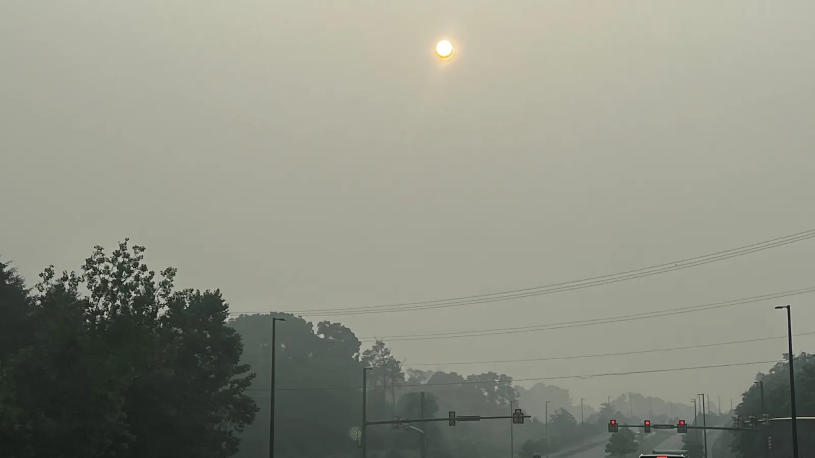 Car red taillights at a traffic light on a street in smog with haze around the sun.