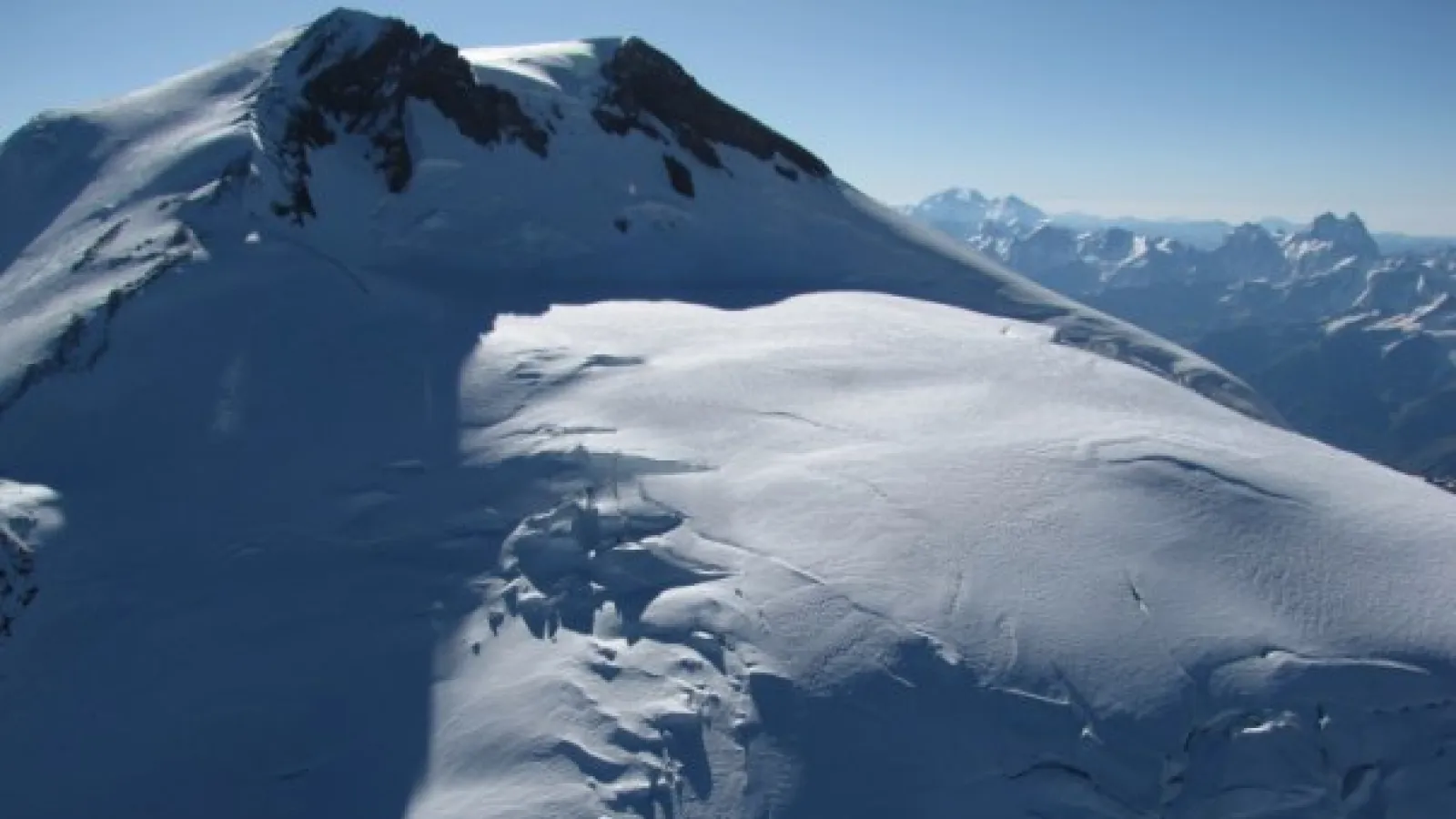 A snow covered mountain with rocky peaks under blue skies.