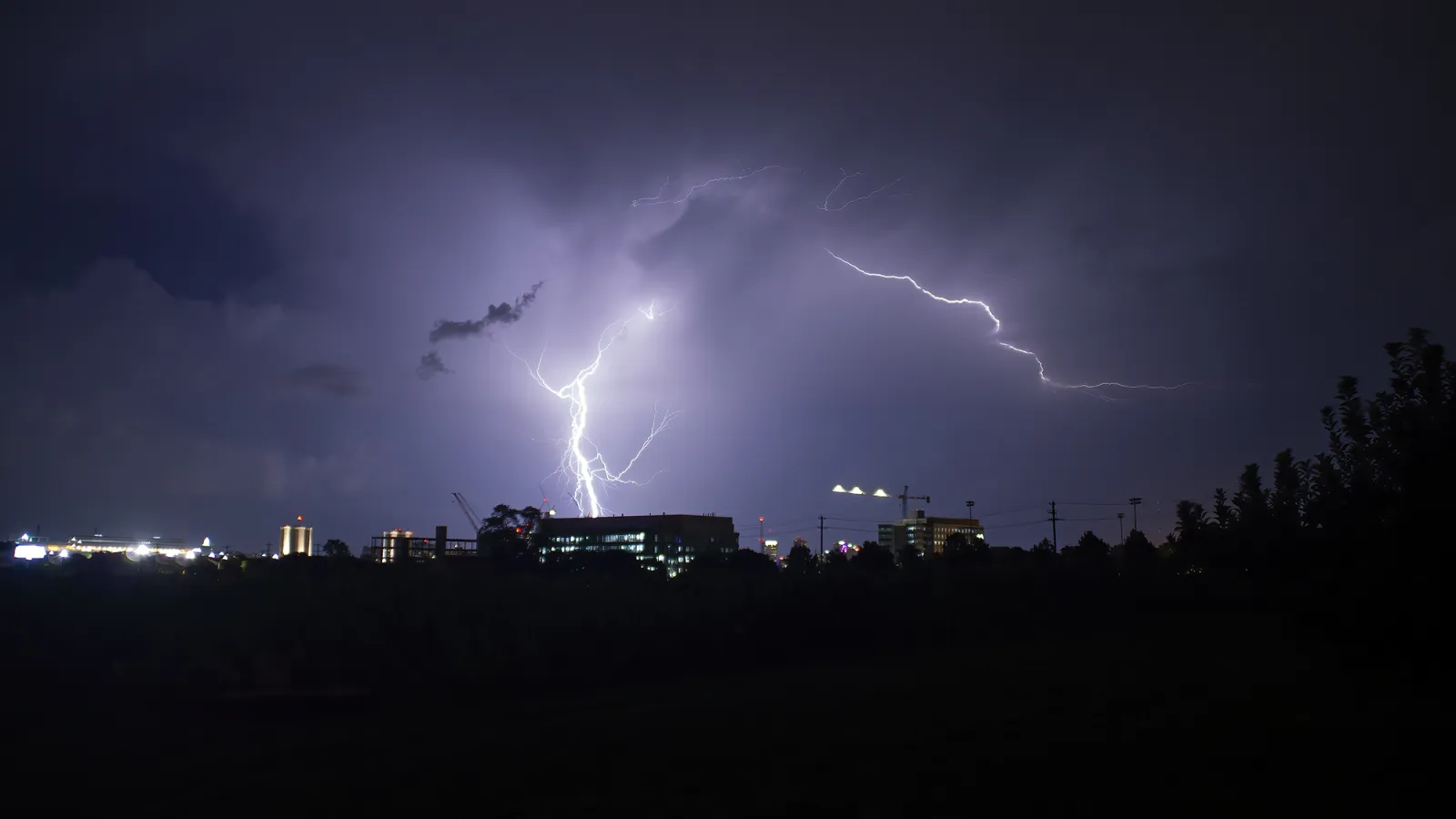 A stormy night, a glowing white lightning strike in the center of the image illuminating the shadowed surroundings.