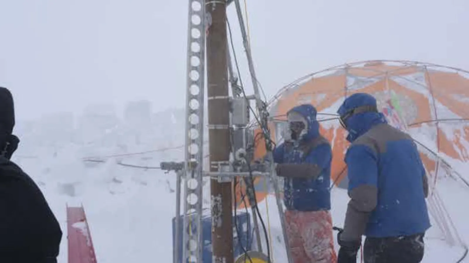 People outdoors in front of an orange tent in snow working with equipment.
