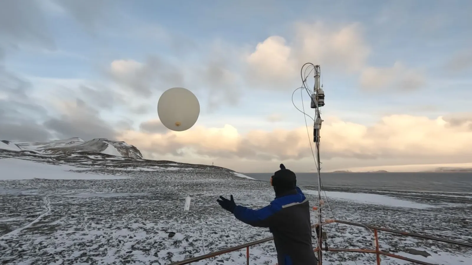 A person releasing a weather balloon into the sky from a snowy landscape during sunrise or sunset.
