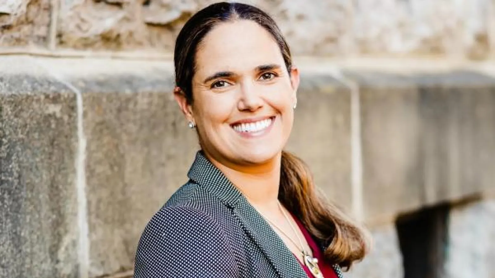 Top half of a person wearing a jacket outdoors, posing smiling partly turned to the camera.