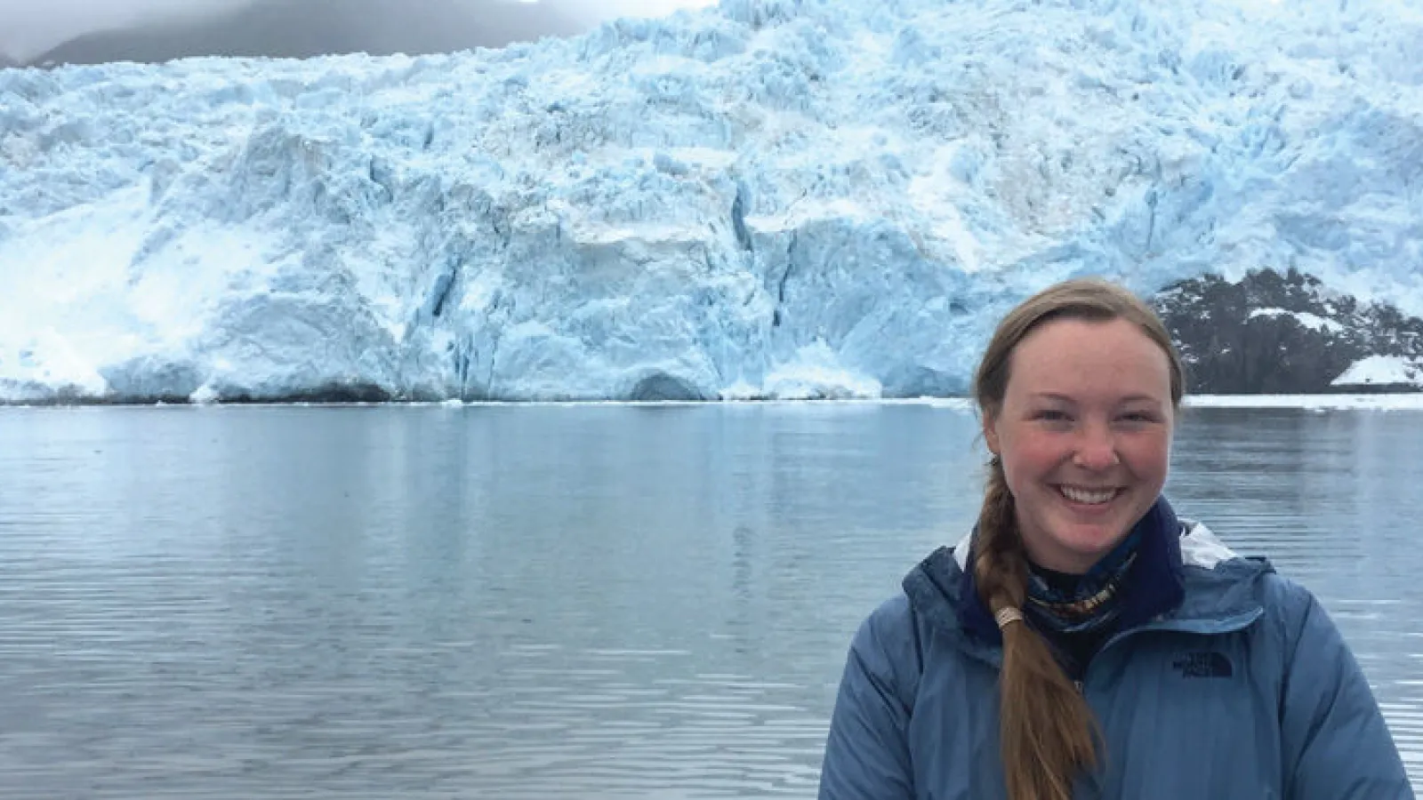 Person smiling in front of a large glacier.