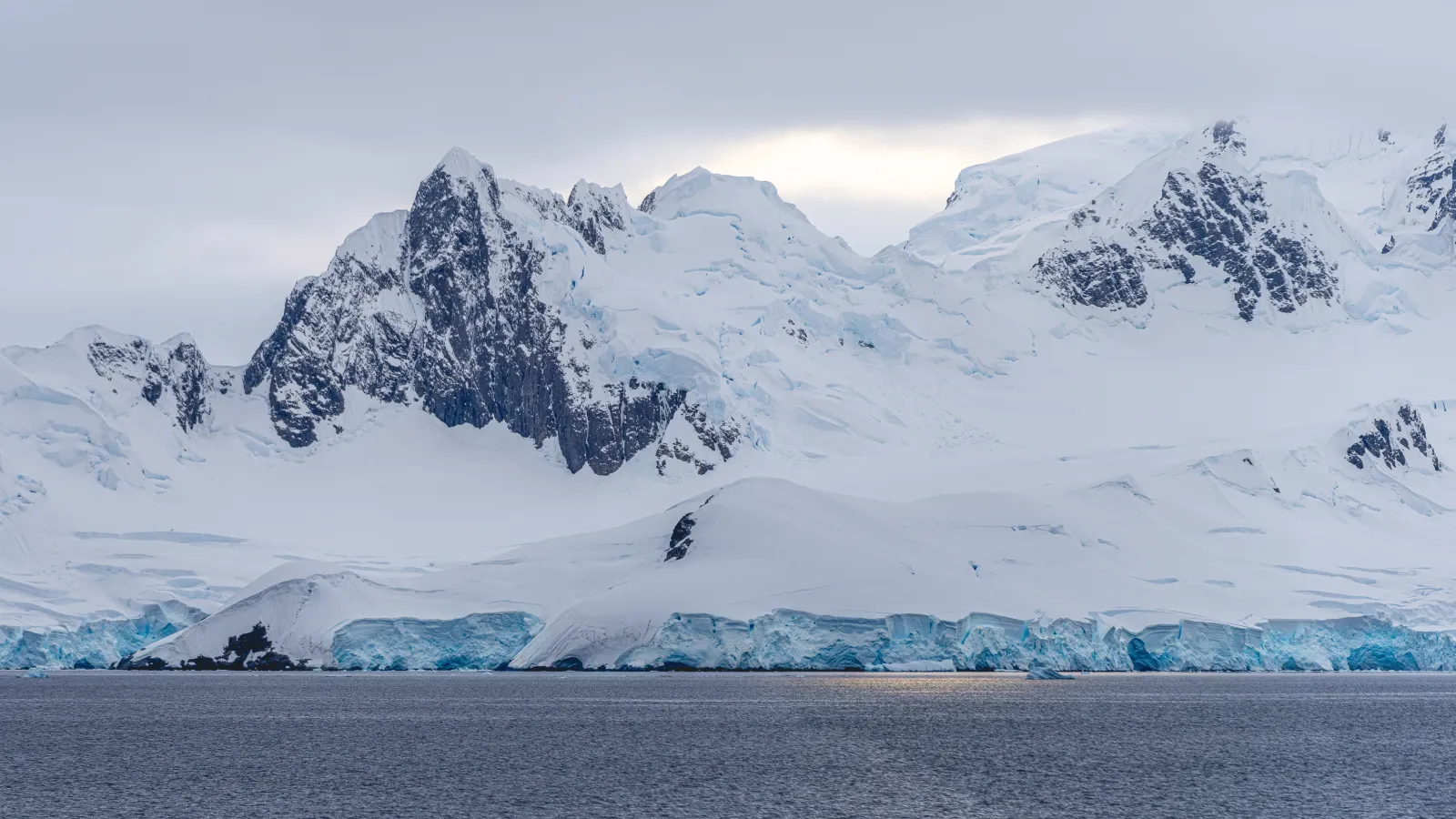 Panoramic view of Antarctica featuring expansive ice-covered mountains under a cloudy sky.