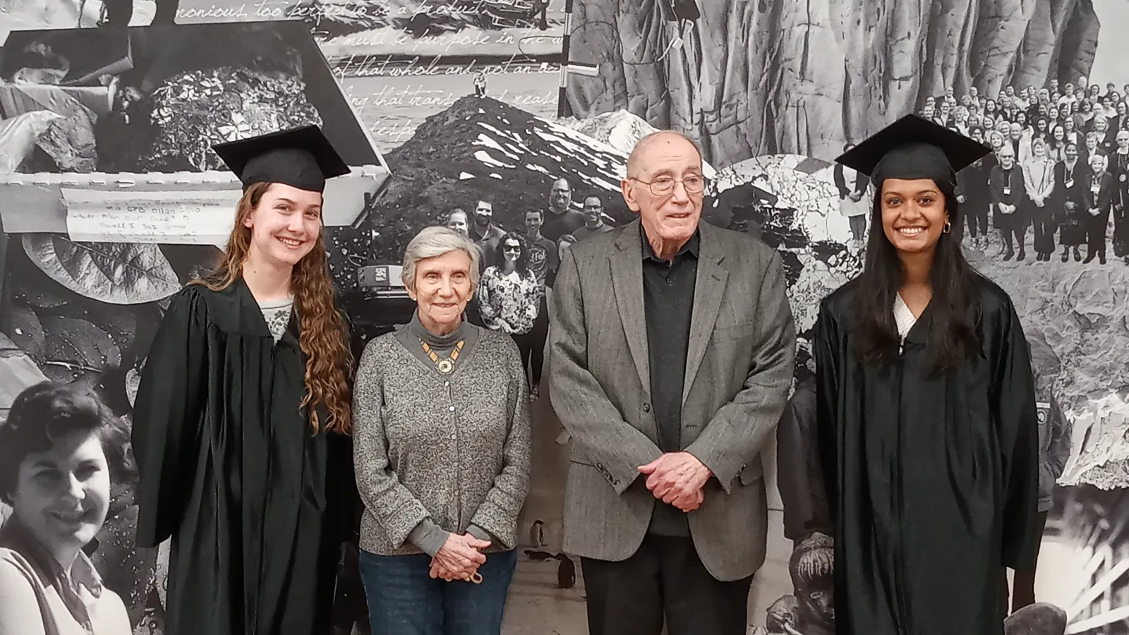 Two people in caps and gowns flank two adults in front of a photo montage.
