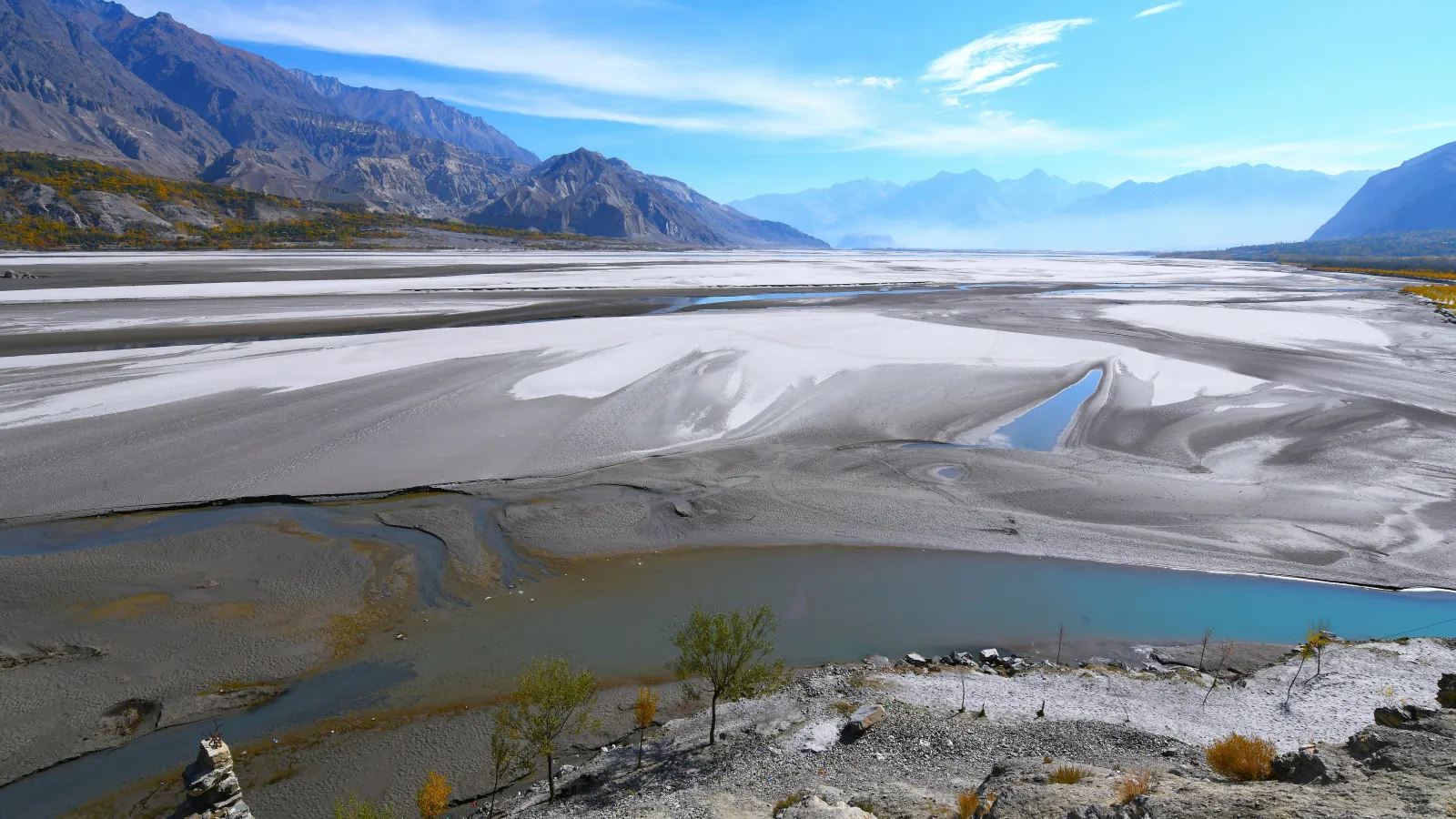 Panoramic view of a Valley showing expansive white flats, winding rivers, and distant mountains under a clear blue sky.