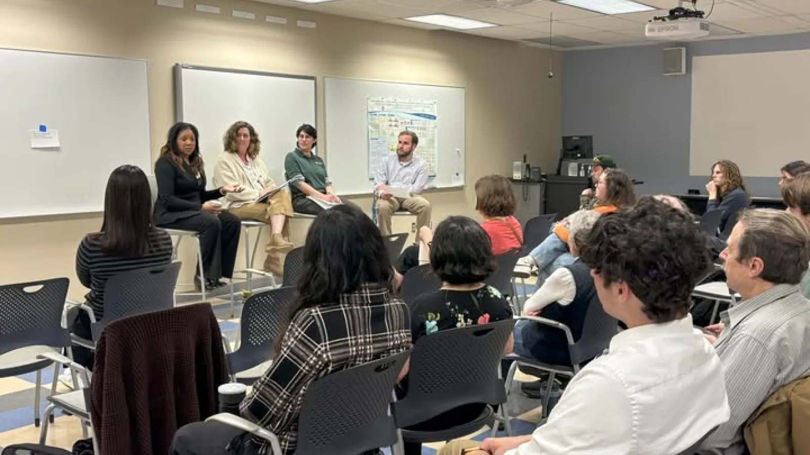 Four panelists  are seated in front of a classroom, engaging with an attentive audience during a discussion.