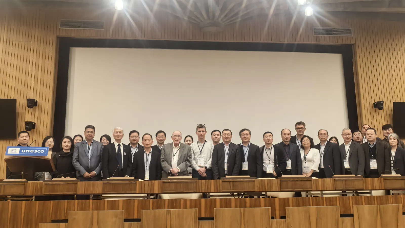 Group of individuals posing for a photo in a conference room with a UNESCO podium.
