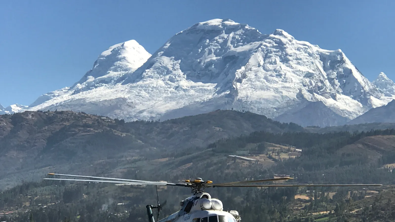A helicopter parked on a tarmac with a mountain in the background under a clear blue sky.