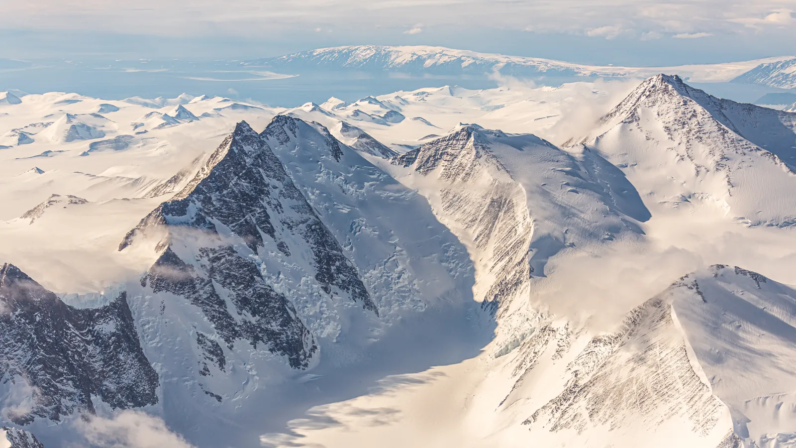 A mountain range covered in snow and ice under blue skies.