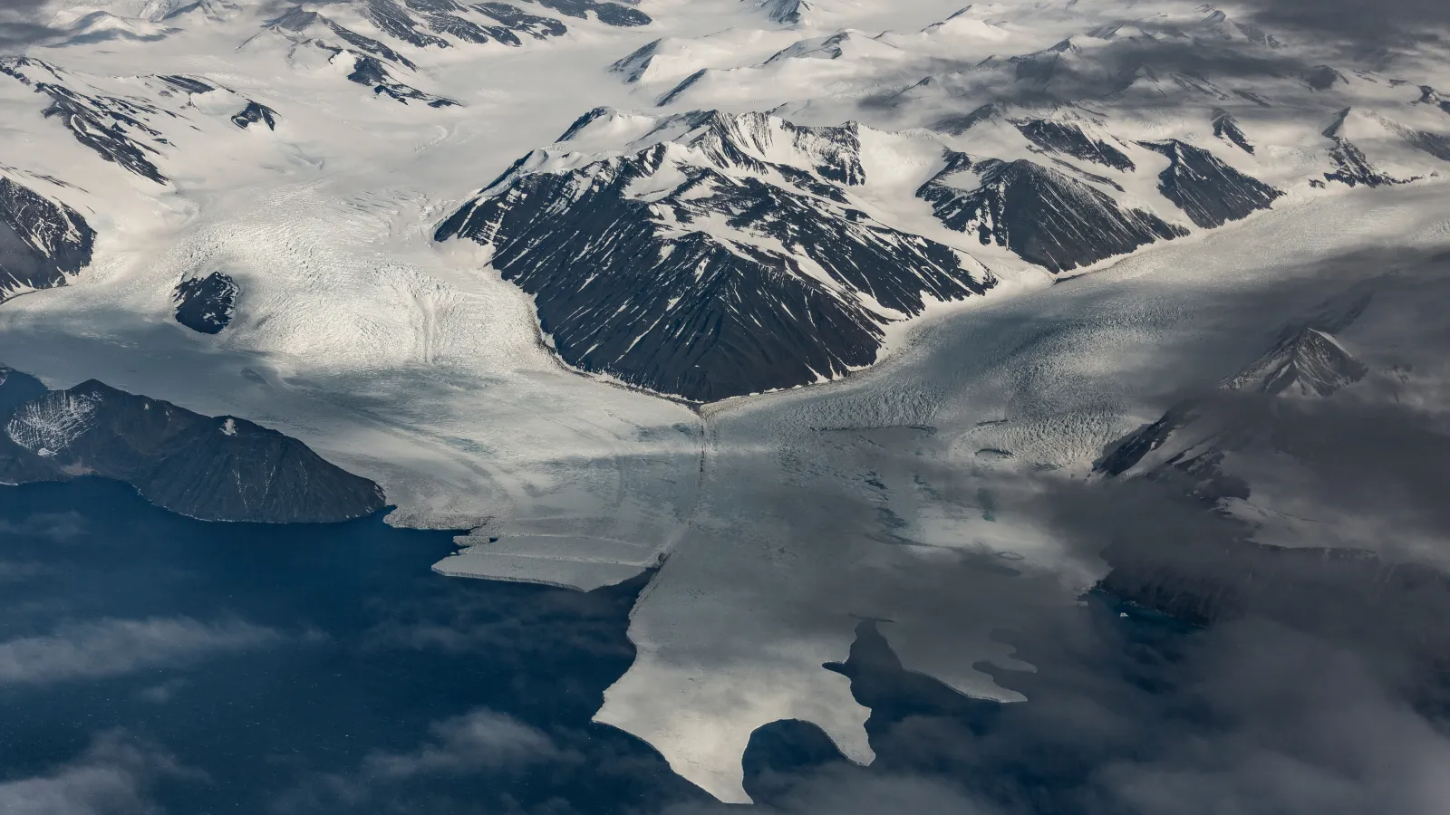 Here’s a short version for social media accessibility:  **Short alt text:** Glacier flowing between dark mountains into the ocean under clouds.