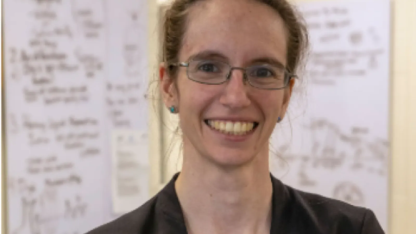 Portrait of a smiling woman with glasses and pulled-back hair, wearing a dark blaze