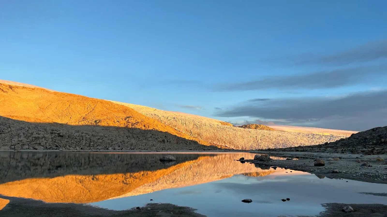 Sunrise reflects golden light on a rocky mountain slope across a still lake.