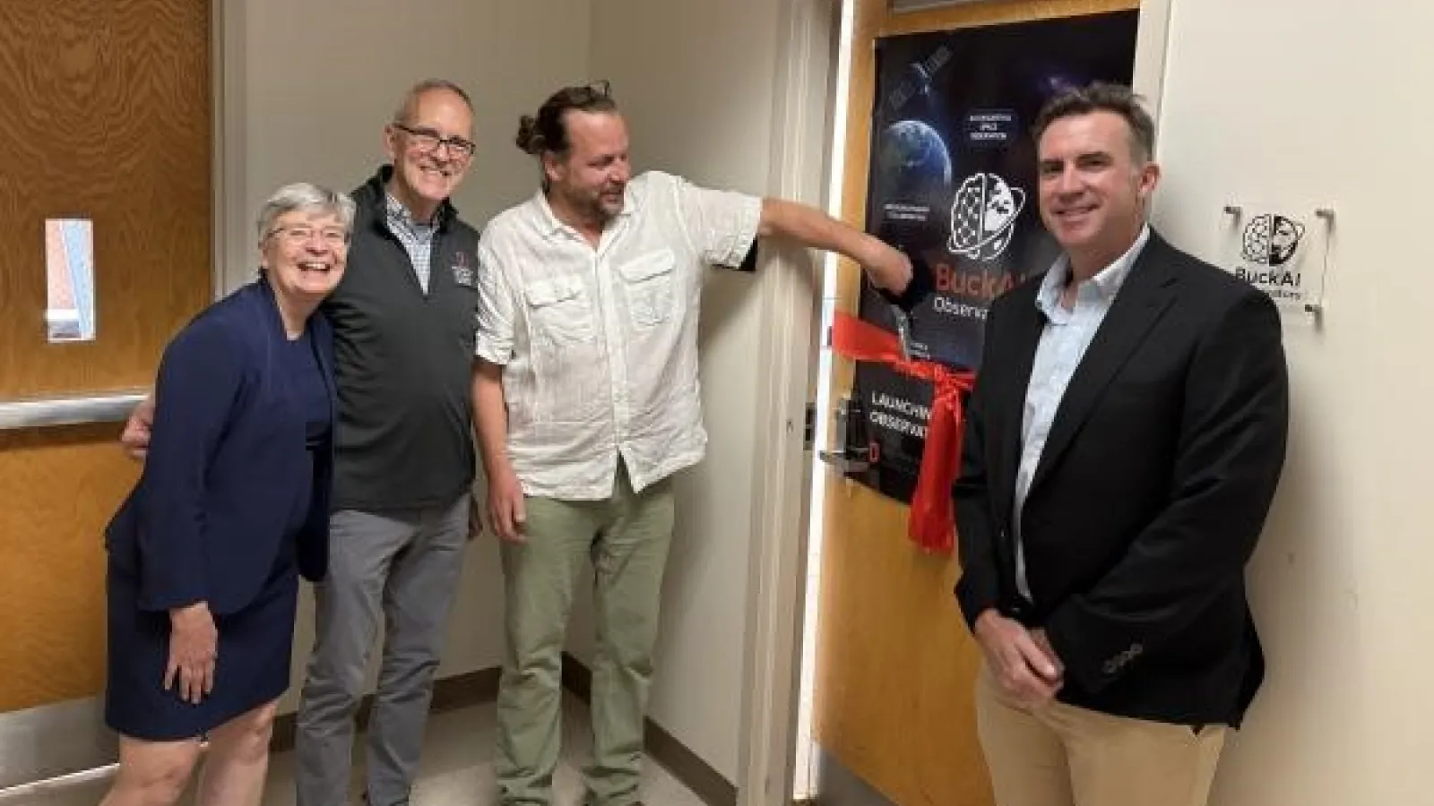Four people stand smiling in a hallway during a ribbon-cutting ceremony