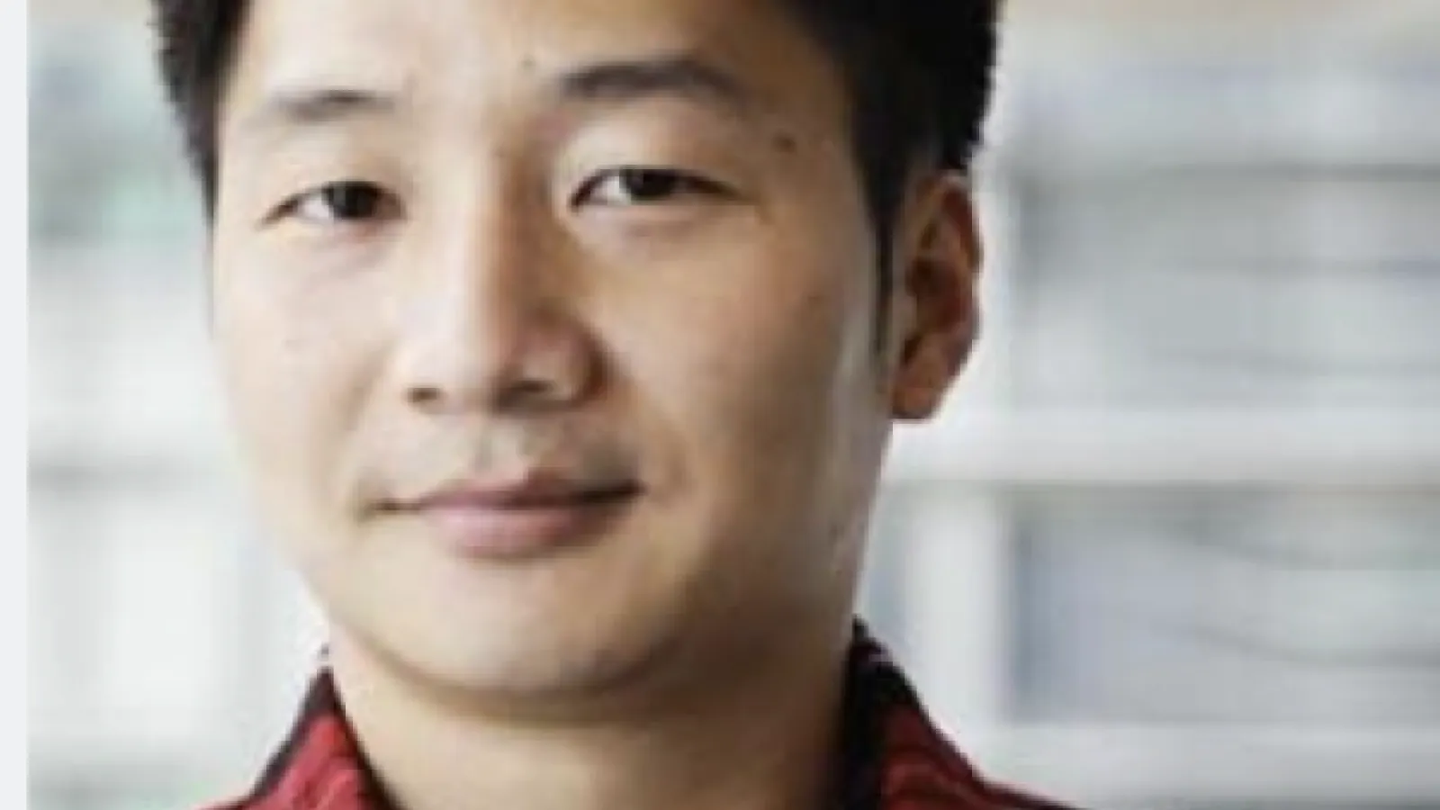 Portrait of a man with short black hair wearing a red and black plaid shirt..