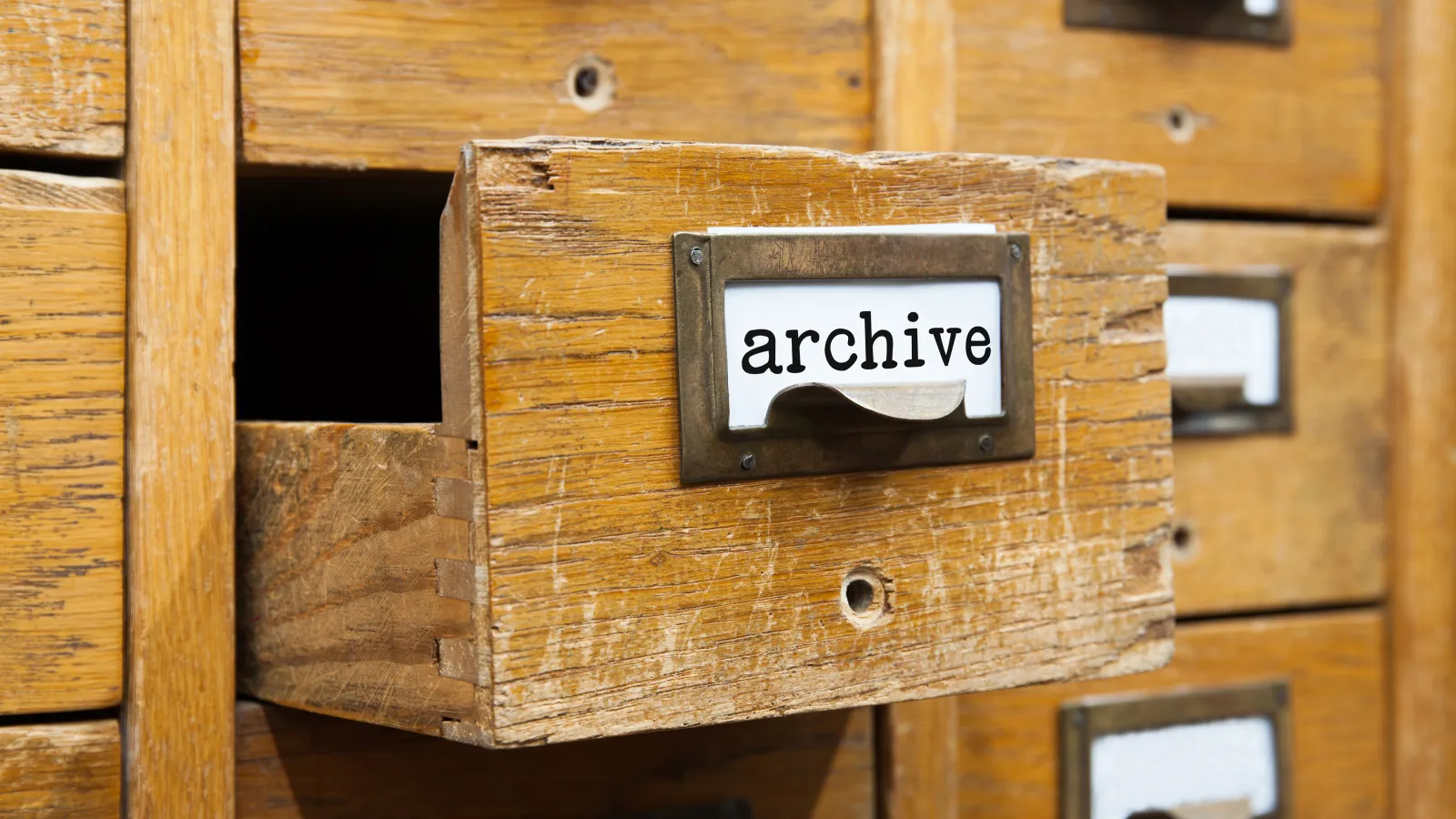 A  wooden filing cabinet with many drawers. on one drawer there is a white background with black lettering saying Archive.