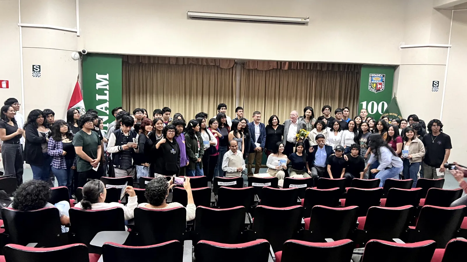 Group photo of students and faculty gathered at the front of an auditorium after a lecture.