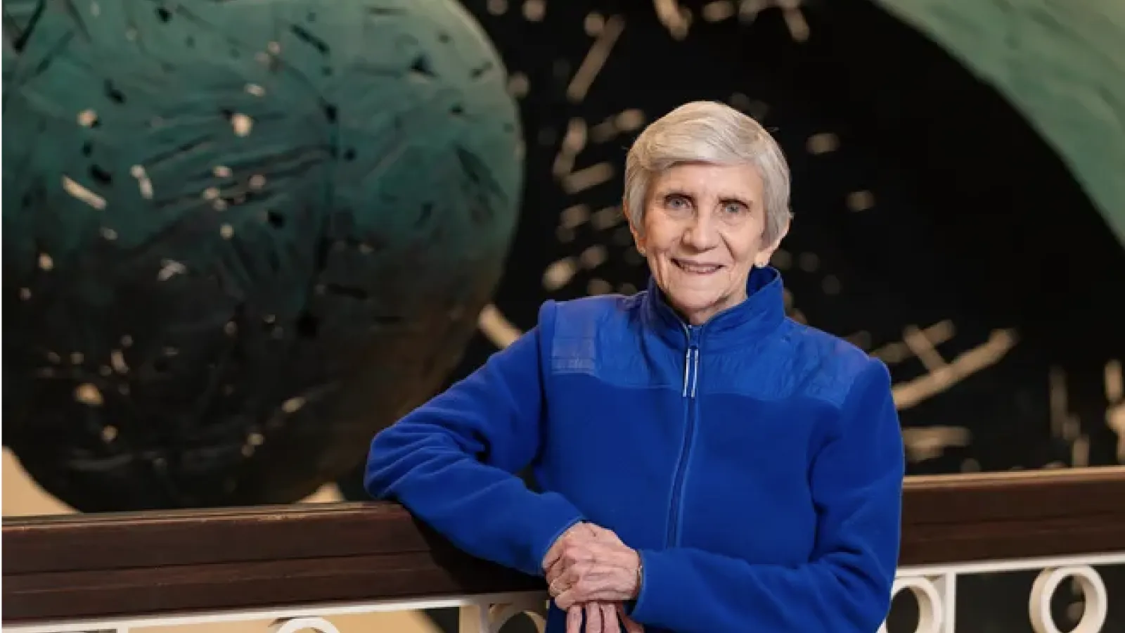 Ellen Mosley-Thompson smiling wearing a bright-blue zip-up jacket leaning against a railing.