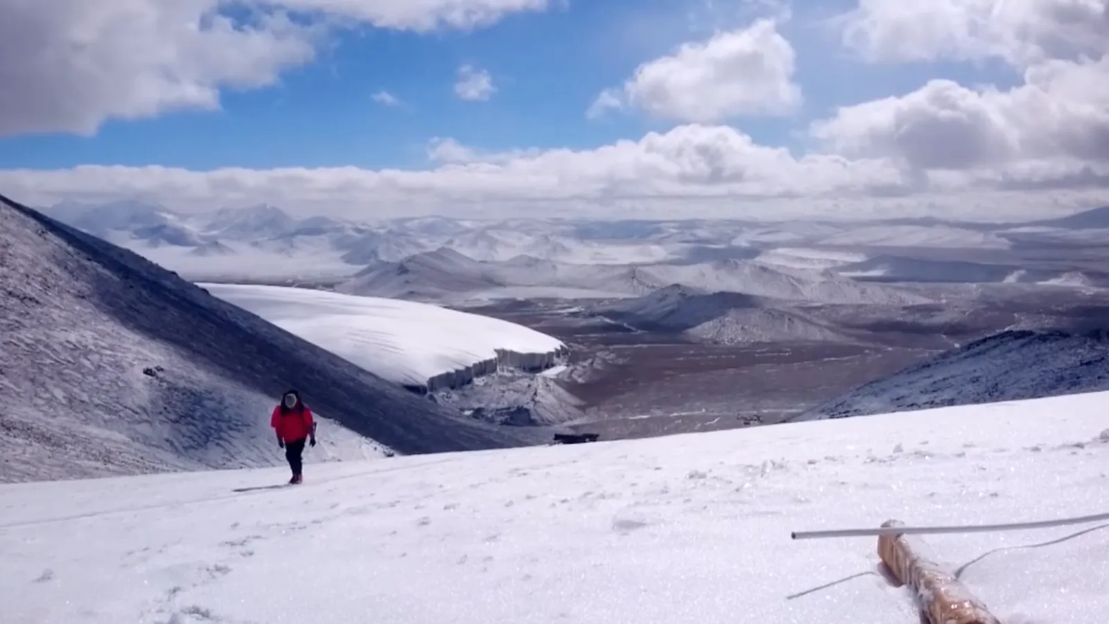 Man walking up glacier with valley and mountains