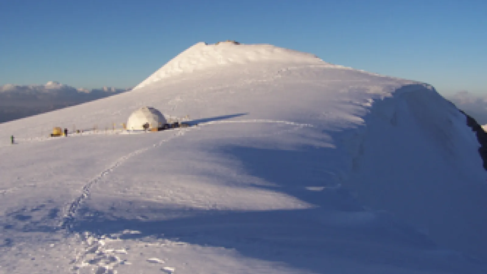 Tent on a mountain glacier with footprints in the snow
