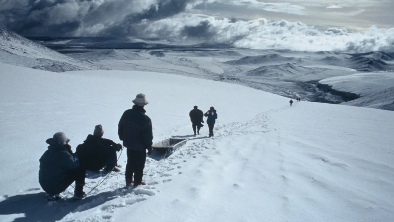 People walking on a snow covered path with a sled under gray skies.