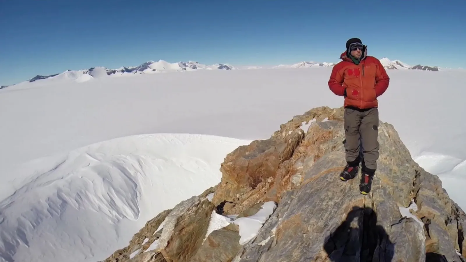 Man standing on a stone peak overlooking a barren snow plain