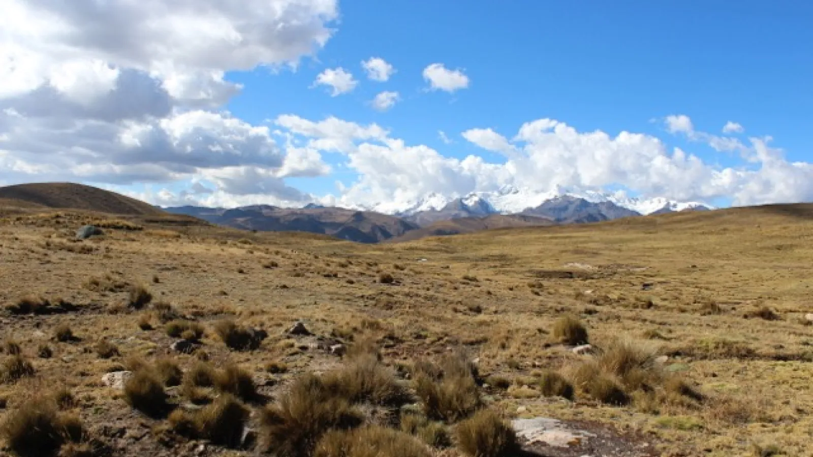 A rolling plain under a cloudy blue sky with mountains far in the distance framing the border between them.