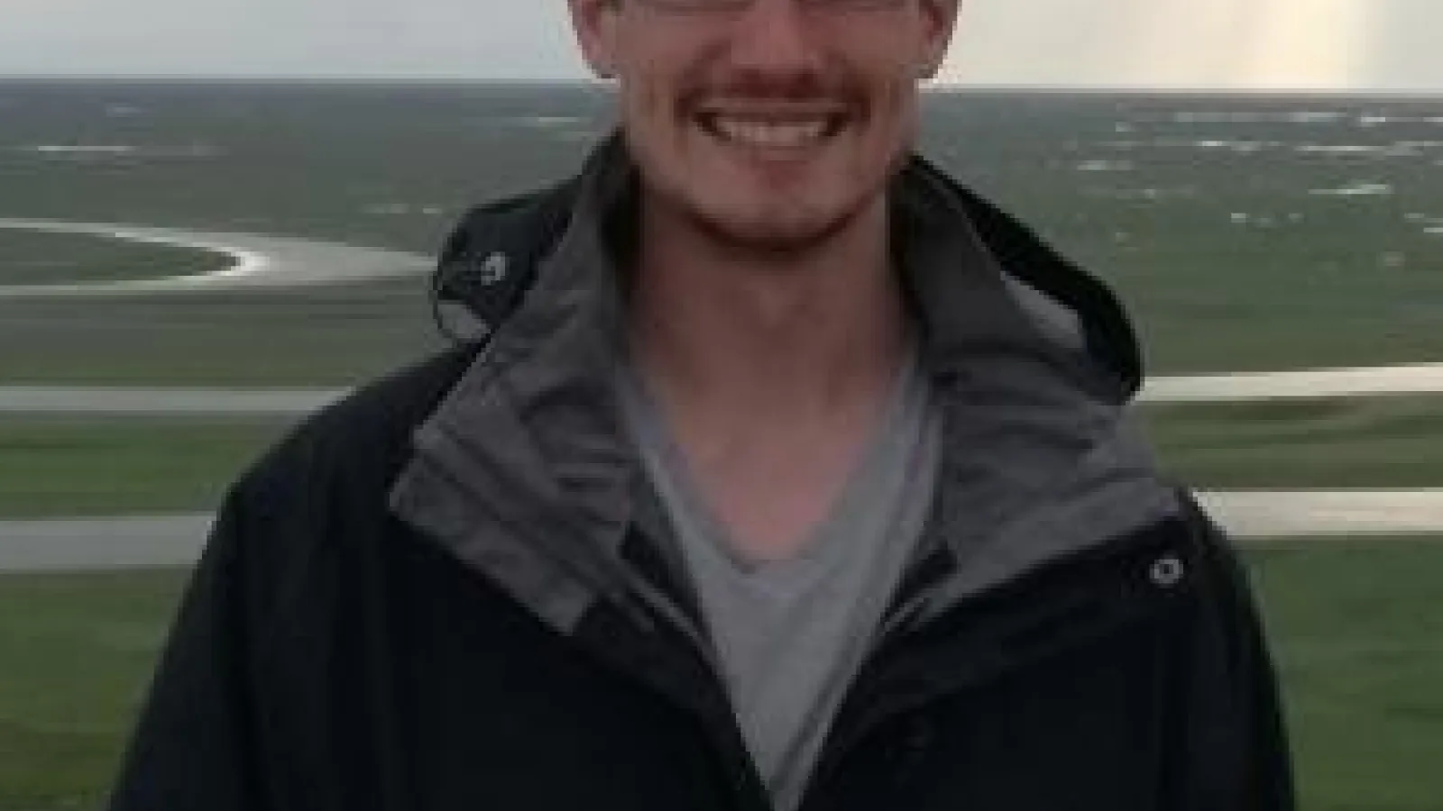 Man standing and smiling in front of river 