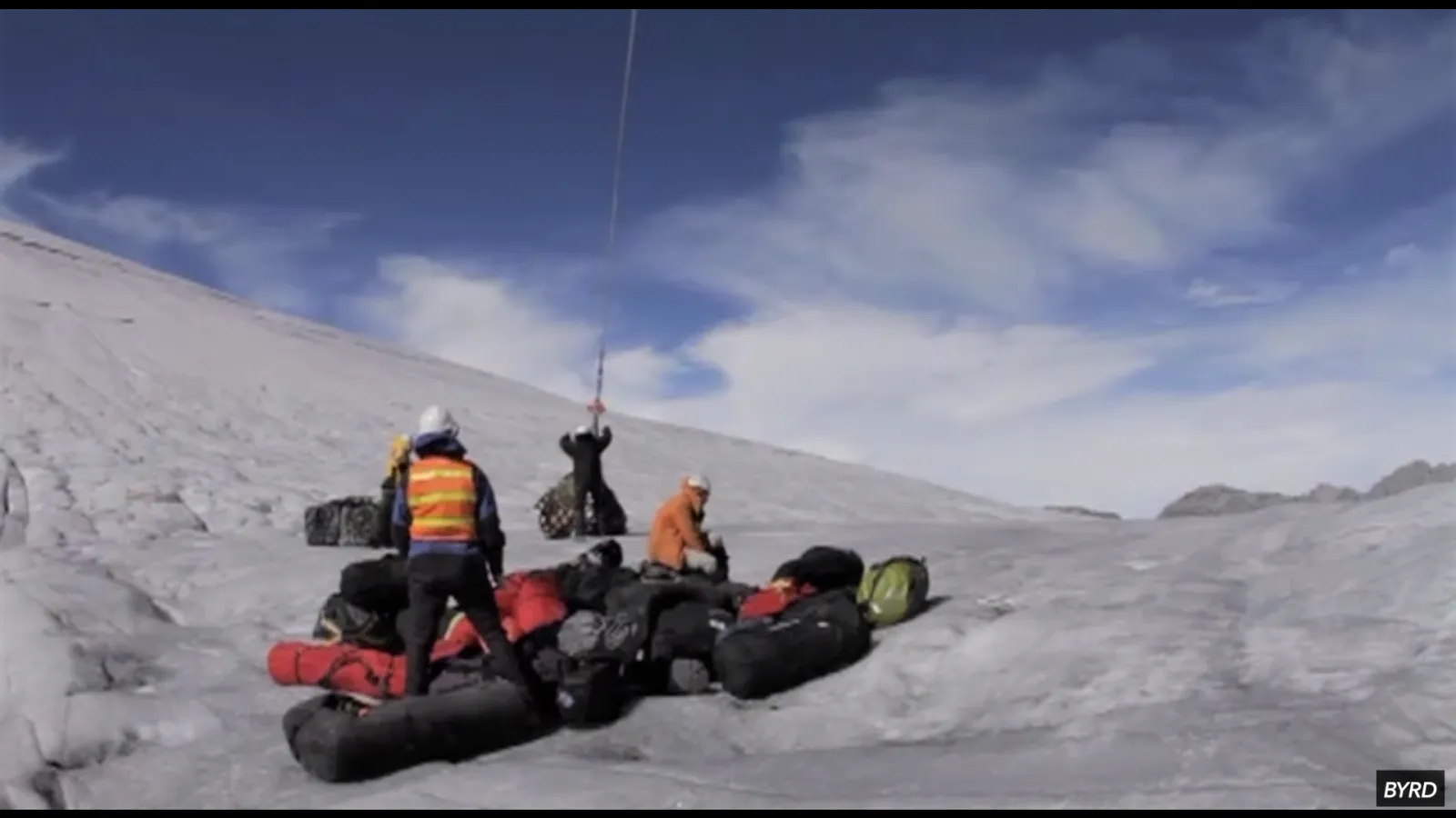 Researchers in winter gear are delivered supplies on snow via helicopter