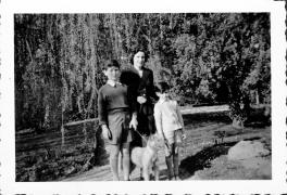 A woman and two young boys standing in a garden with a fluffy dog between them