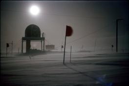 The image is lit by the bright moon. A round, raised tower is visible, as it another raised square tower in the distance. Other ropes and poles are visible through the misty light.