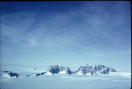 Two rocky mountains peaking through the snow with a great, blue sky with wispy clouds behind them