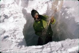 Henry Brecher digging in a green jacket. He is standing in the partially dug out pit with a shovel throwing snow behind his back.