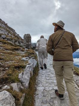 Henry and Gabriel hiking up a steep stone path with grassy mountain on either side. Henry is walking in front.