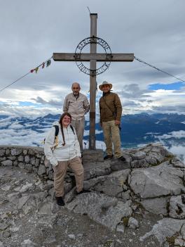 Emily, Henry, and Gabriel standing on the edge of the mountain, the sky white and the mountain blue behind them.