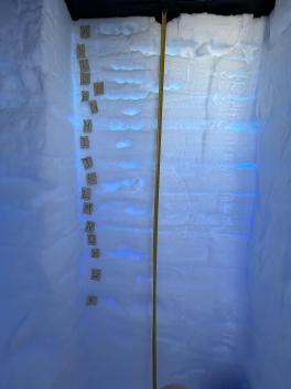 A wall of snow on three sides with a measuring tape in the middle with alphabet a-R posted to the left on the wall.