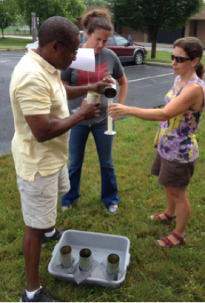 three people conduct a small experiment outside in the grass