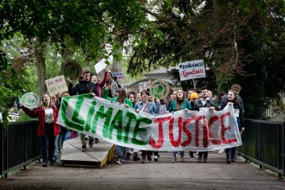 A group of protesters outdoors holding a long banner that has the word climate  in green and justice in red.