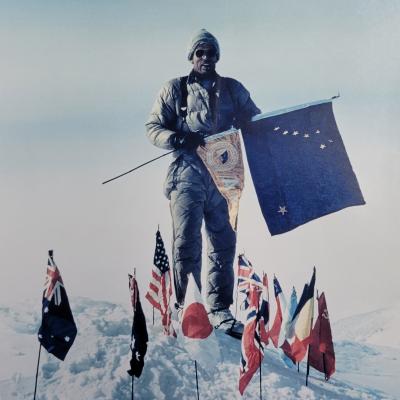 A man holding a flag and standing in the snow with many small flags around him on the ground. 