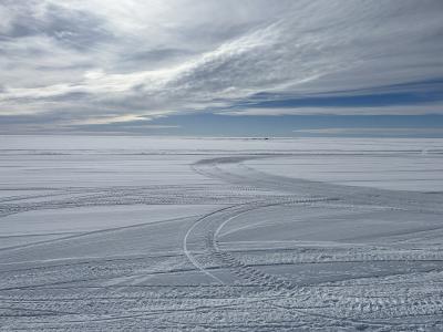 Vast field of snow under blue skies with white clouds.