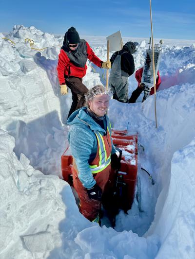 A group of people in multiple dug up ditches working on equipment in the snow.