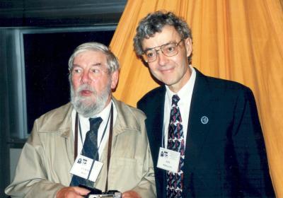 Two men posing indoors,  in front of an orange fabric.